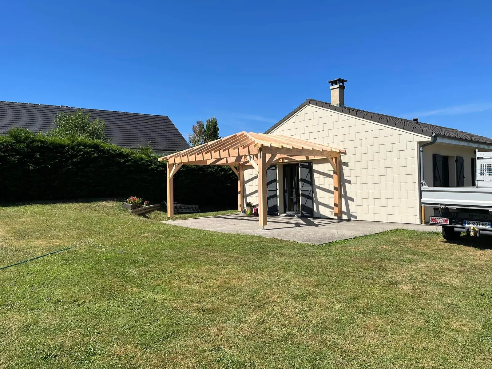 Structure d’auvent en bois au milieu d’une pelouse, devant une maison