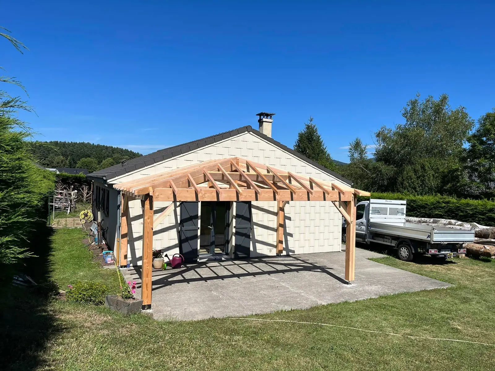 Auvent en bois couvert de tuiles devant une maison, vu depuis la pelouse