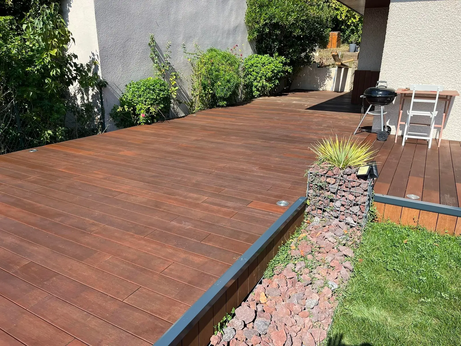 Terrasse en bois posée au bord d’une pelouse, bordure en gabion