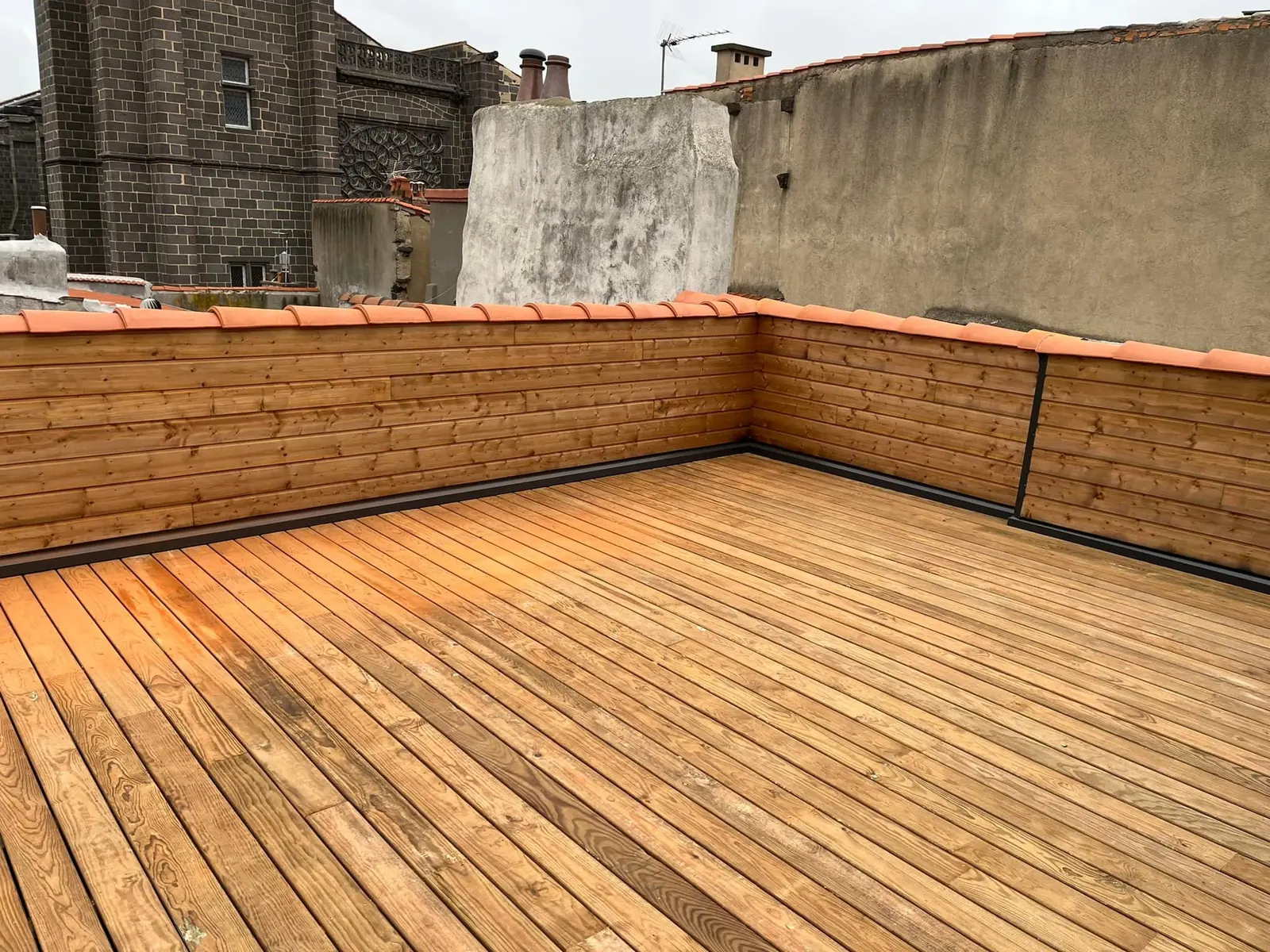 Terrasse en bois posée en toiture, entre les murs de la ville